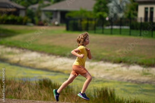 Young kid running and smiling in the park. Active little kid running along street during leisure sport activity. Sporty kid running in nature. Child run. Kids running. Summer sport. Happy childhood.