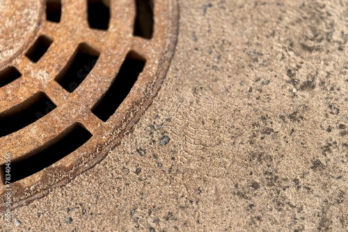 A rusty iron hatch with a pattern above an observation well is located on auto road in daytime. Close-up