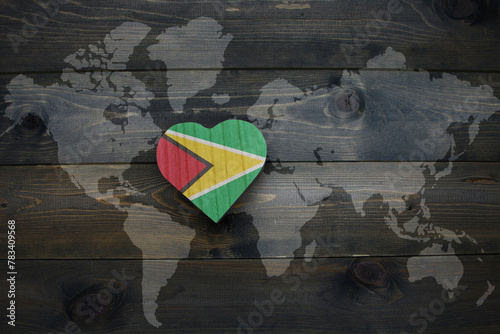 wooden heart with national flag of guyana near world map on the wooden background. photo