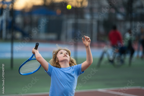 Kid playing tennis on court. Child hit tennis ball with tennis racket. Active exercise for kids. Summer activities for children. Child learning to play tennis. Sport Kid hitting Ball on court.