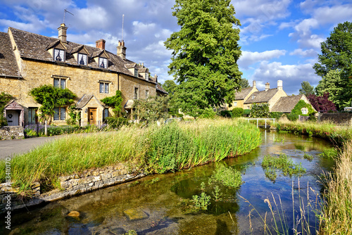 Beautiful Cotswolds village of Lower Slaughter with river under blue skies, Gloucestershire, England
