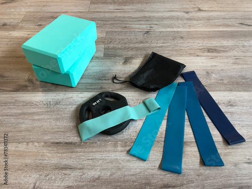  Fitness equipment for Yoga Pilates on wooden floor: green Yoga Blocks, blue Resistance Bands and Rubber Weight Plate
