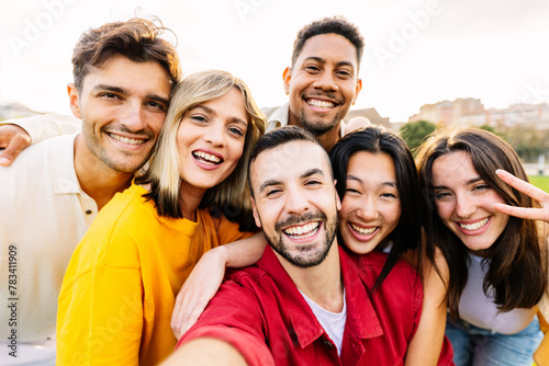 Young community concept with millennial friends having fun together outdoors. Diverse group of millennial people taking selfie portrait enjoying free time at city park.