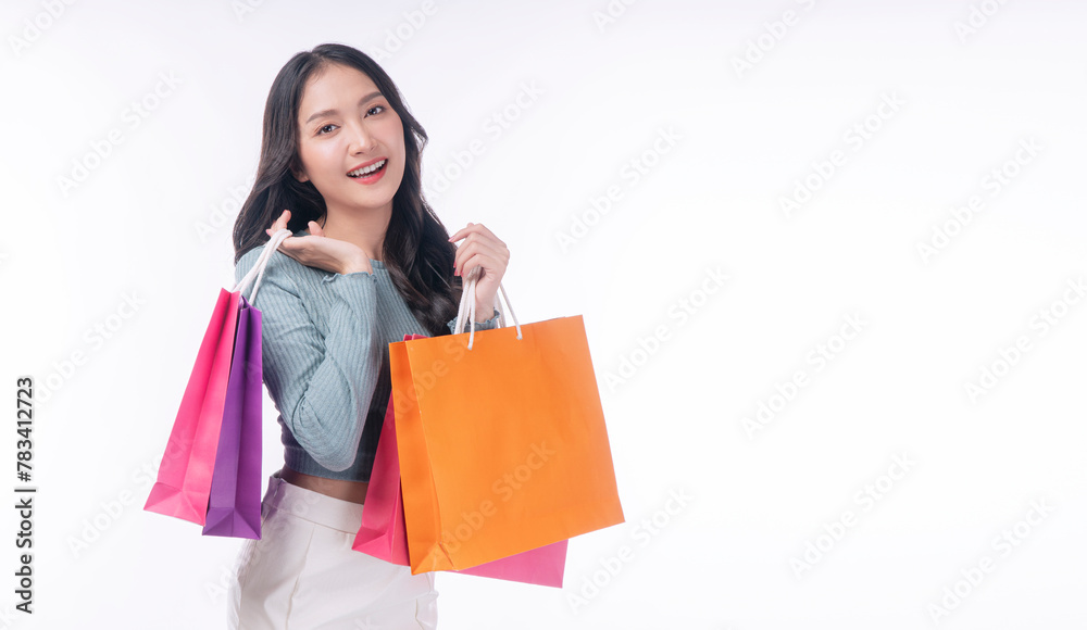 Enjoyment excited asian woman carry shopping bags standing on white background. Trendy happy shopper consumer carefree young girl holding shopping paper bags with copy space over isolated background. Enjoyment excited asian woman carry shopping bags standing on white background. Trendy happy shopper consumer carefree young girl holding shopping paper bags with copy space over isolated background.