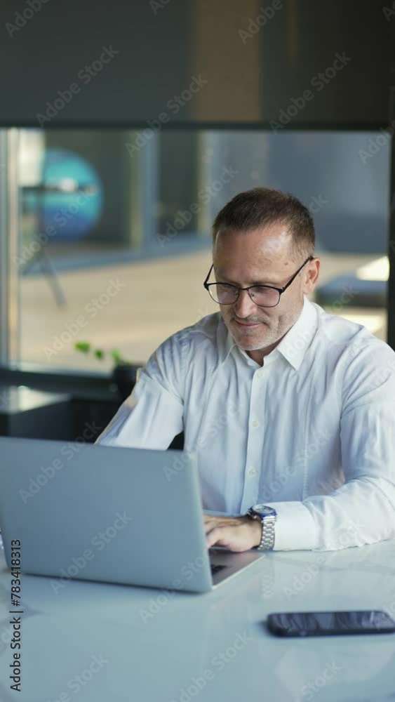 Smiling businessman working on laptop computer at home office. Male professional typing on laptop keyboard at office workplace. Portrait of positive business man looking at laptop screen indoors Smiling businessman working on laptop computer at home office. Male professional typing on laptop keyboard at office workplace. Portrait of positive business man looking at laptop screen indoors