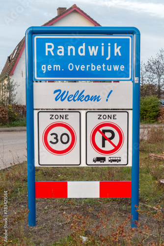 Place name sign for the village of Randwijk, municipality of Overbetuwe, the Netherlands, with the text 'welcome' under it (also no parking for trucks or buses and a speed limit of 30 km per hour) photo