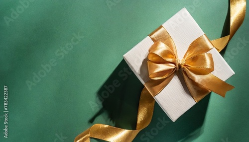 top view of open gift box or present box with gold ribbon and bow on green background with shadow