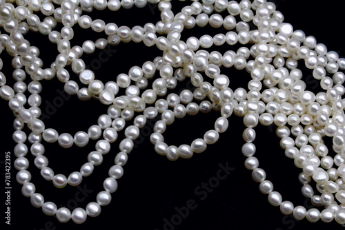 Chinese round freshwater white pearls on strands ready to become a necklace, some of the favorite materials for jewelry on black background. Lustrous nacre forms an organic gem.
