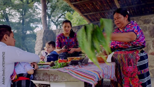 A mature Latina woman of the Mayan ethnic group leads the family to participate in the preparation of organic corn tamales.