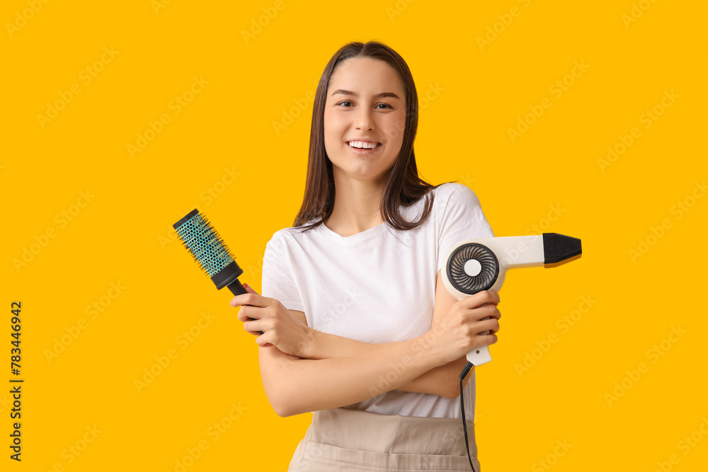 Female hairdresser with dryer and brush on yellow background Female hairdresser with dryer and brush on yellow background