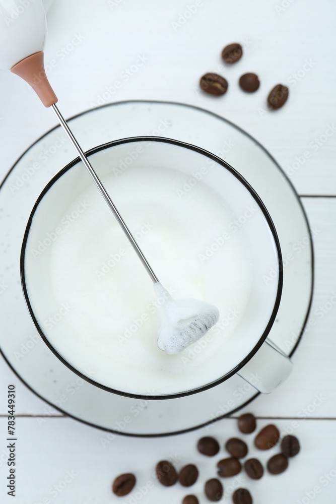 Mini mixer (milk frother), whipped milk and coffee beans on white wooden table, flat lay Mini mixer (milk frother), whipped milk and coffee beans on white wooden table, flat lay