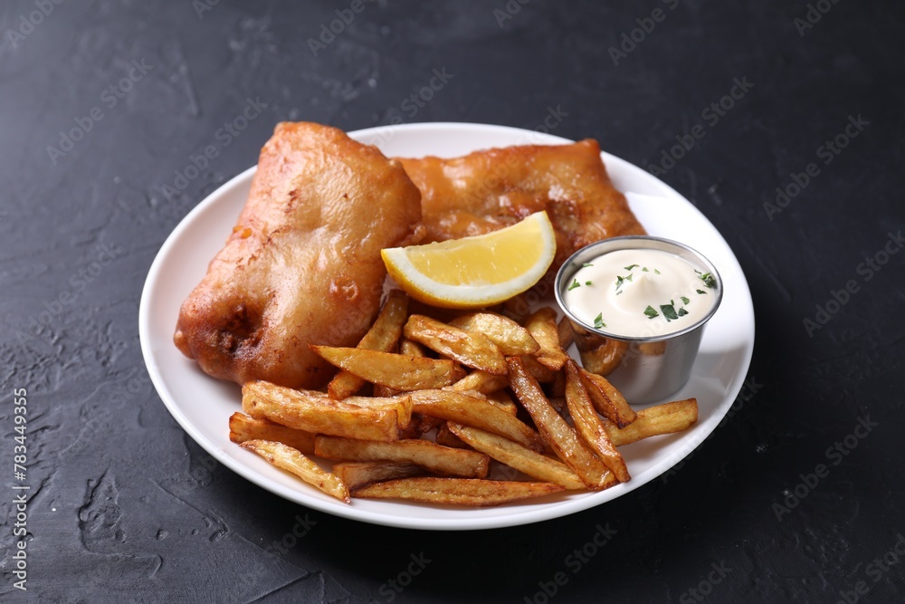 Tasty fish, chips, lemon and sauce on black table Tasty fish, chips, lemon and sauce on black table