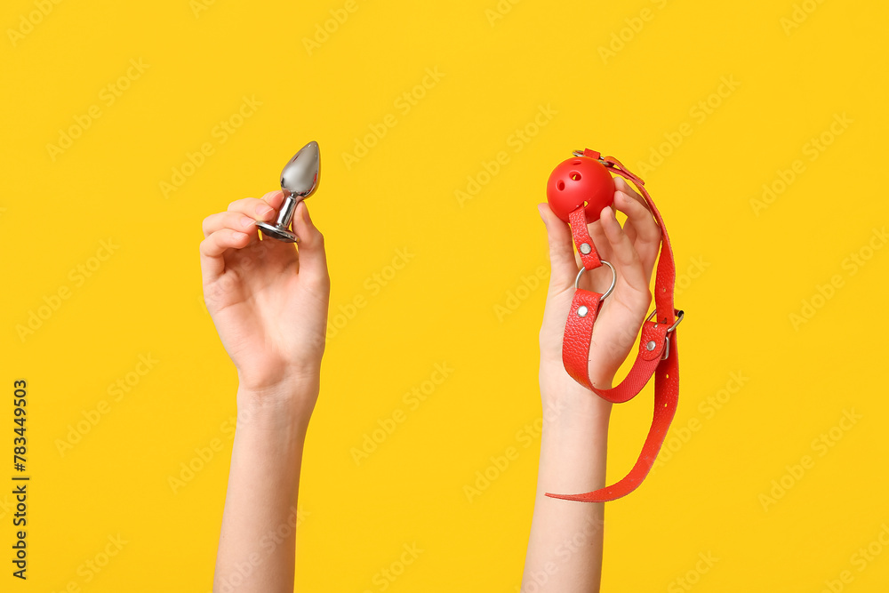 Female hands with anal plug and gag on yellow background, closeup - obrazy, fototapety, plakaty 