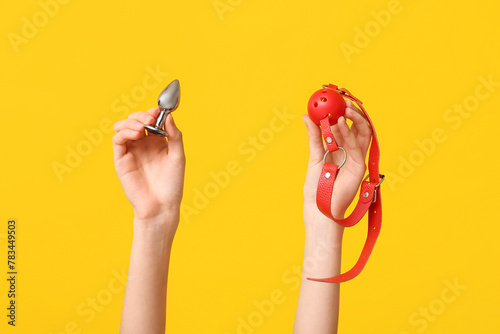 Female hands with anal plug and gag on yellow background, closeup photo