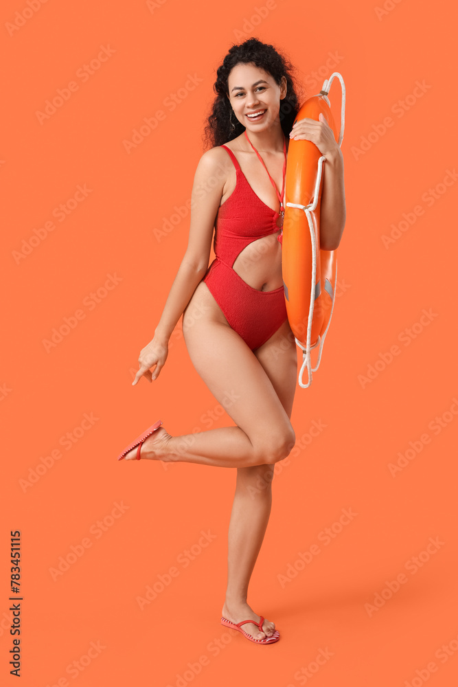 Beautiful young happy African-American female lifeguard with ring buoy on orange background - obrazy, fototapety, plakaty 