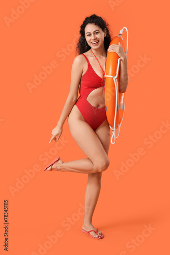 Beautiful young happy African-American female lifeguard with ring buoy on orange background © Pixel-Shot