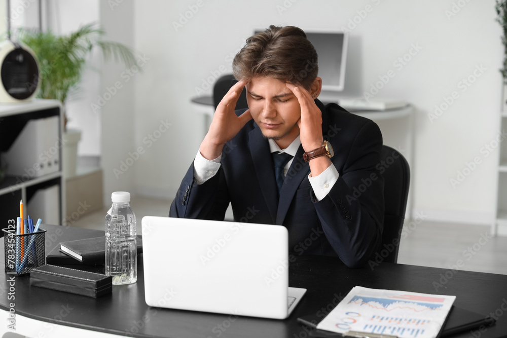 Tired young businessman suffering from headache in office Tired young businessman suffering from headache in office