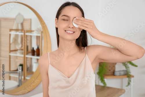 Young woman with cotton pad removing makeup in bathroom