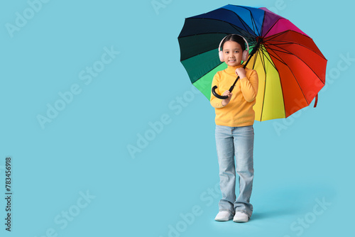 Portrait of fashionable little girl with headphones and umbrella on blue background