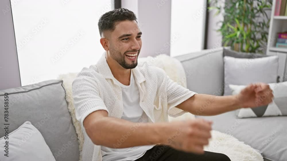 Excited young arab man with a joyful smile, celebrating victory on his sofa at home. yes! arms raised, expressing the happiness of a triumphant win. Excited young arab man with a joyful smile, celebrating victory on his sofa at home. yes! arms raised, expressing the happiness of a triumphant win.