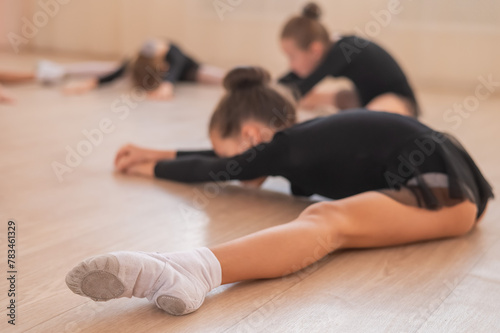 Girls ballerinas stretch while lying in a wide fold. 