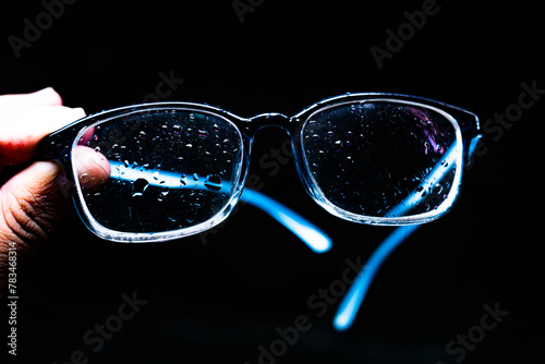 A person is holding a pair of glasses with water droplets on the lenses