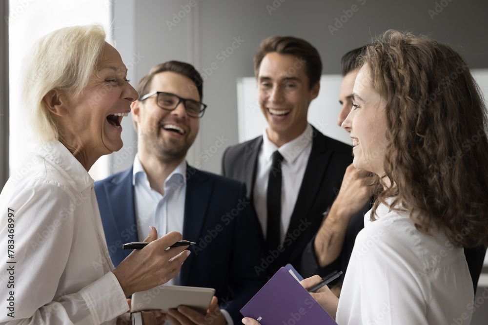 Fototapeta premium Cheerful group of businesspeople laughing met in office, stand together in boardroom after profitable deal, discuss business project, enjoy friendly funny conversation, enjoy career growth and success
