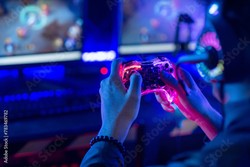 Close-up, video game console controller in gamer hands at colorful neon light living room at night, E-sport streaming game online, selective focus
