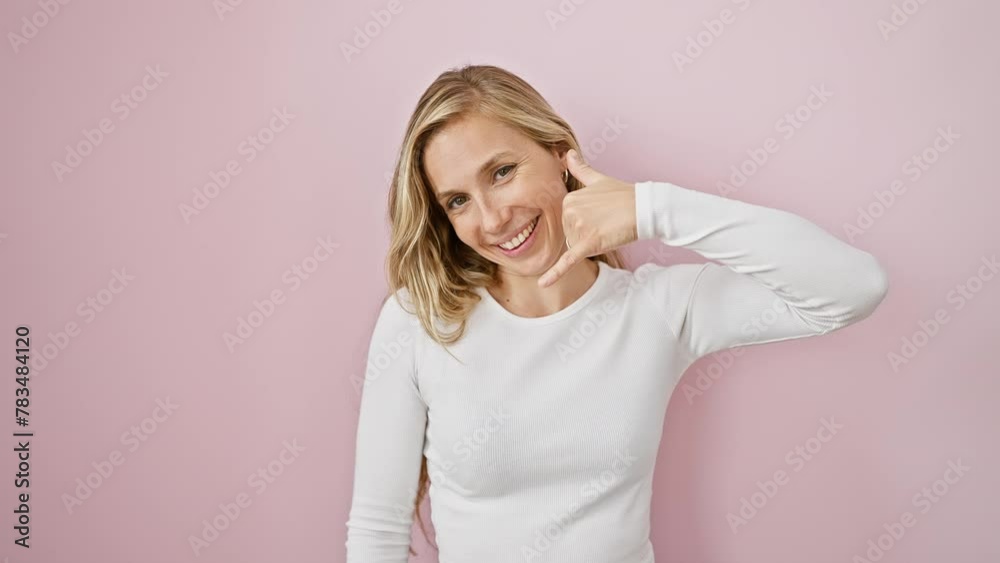 Cheerful young blonde woman making a cool phone call gesture, smiling over isolated pink background, friendly communication concept Cheerful young blonde woman making a cool phone call gesture, smiling over isolated pink background, friendly communication concept