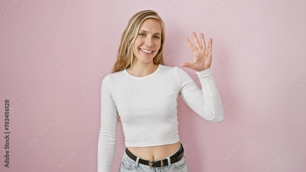 Cheery and self-assured, a young blonde woman joyfully flashes the number five with her fingers, posing confidently against a vivacious pink backdrop. Cheery and self-assured, a young blonde woman joyfully flashes the number five with her fingers, posing confidently against a vivacious pink backdrop.