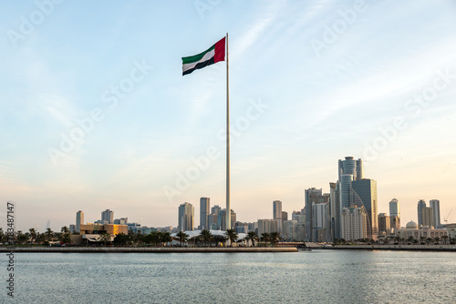 Flag of the United Arab Emirates in Sharjah on coastline in the background of tall skyscrapers. urban landscape