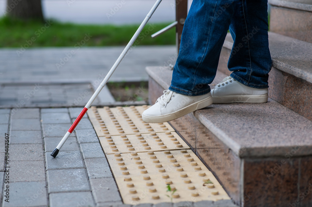 Close-up of female foot, walking stick and tactile tiles. Blind woman walking down stairs using a cane. Close-up of female foot, walking stick and tactile tiles. Blind woman walking down stairs using a cane.
