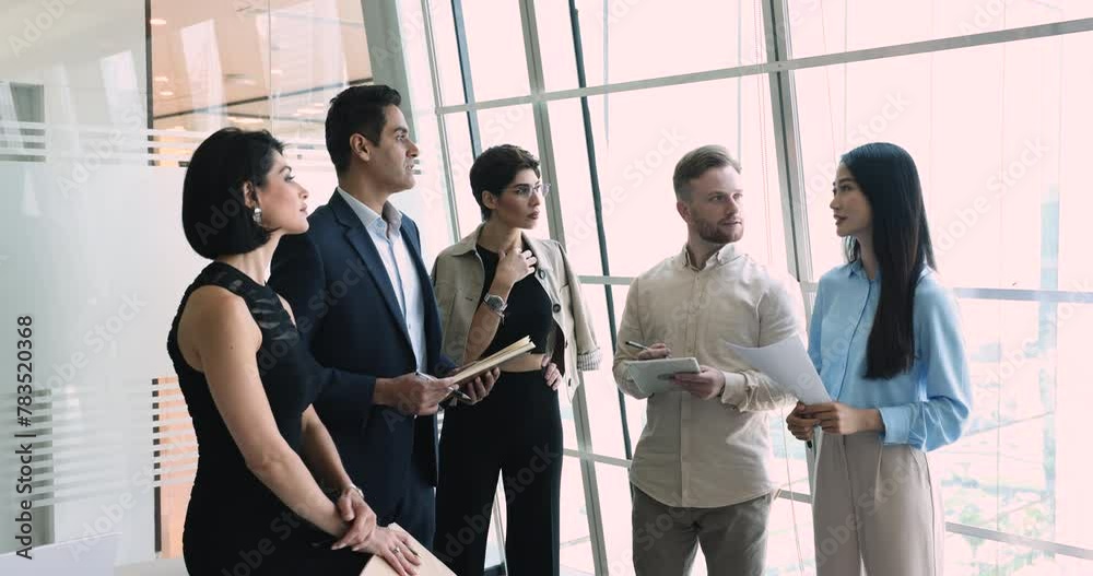 Multiethnic business team of serious coworkers standing at office large window for briefing, talking, discussing work tasks, teamwork strategy, listening to male Indian boss Multiethnic business team of serious coworkers standing at office large window for briefing, talking, discussing work tasks, teamwork strategy, listening to male Indian boss