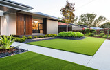 Modern front yard design with artificial grass and walkway, contemporary home exterior with white walls, wooden slats on the sides of windows, minimal garden landscaping, and greenery in small space