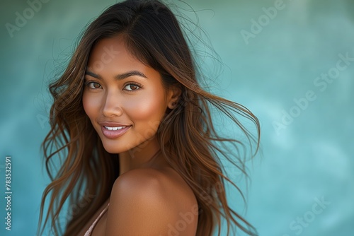Young Asian model smiles at the camera. Gentle gaze from a maiden with disheveled locks, sporting a ruffled garment, in front of a teal wall. photo