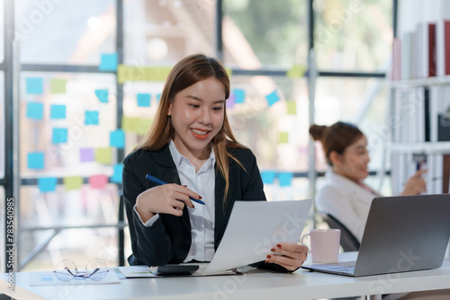 Smiling asian businesswoman analyzing financial documents with pen in hand. Business strategy and analytics concept