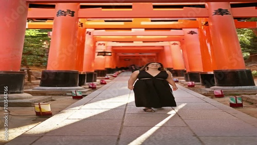 Confident hispanic beauty in glasses, grinning ear-to-ear, looking around in awe at orange-red torii tunnel at fushimi temple in kyoto! photo