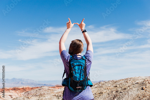 hiker in a purple shirt makes a 'W' sign under the desert sky