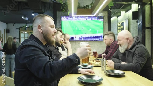 Group of young people, men and women watching match at pub, drinking beer. Fans emotionally cheering up sport team. Celebration of winning game. Competition, championship, match translation.