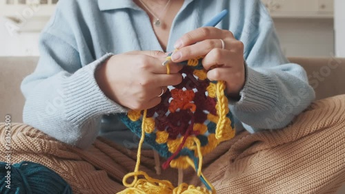 Young woman knitting crocheting with colored yarn granny square at home. Woman doing needlework, home hobbies