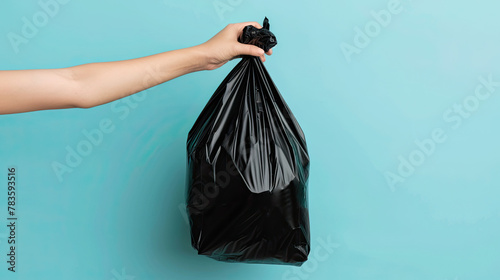 Hand holding full black garbage bag on pastel blue background