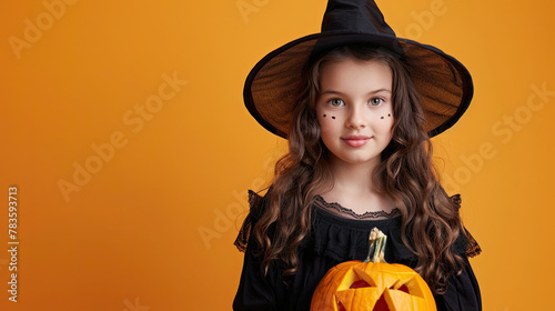 Magician young girl wearing black costume and halloween makeup holding carved pumpkin , isolated on orange background 