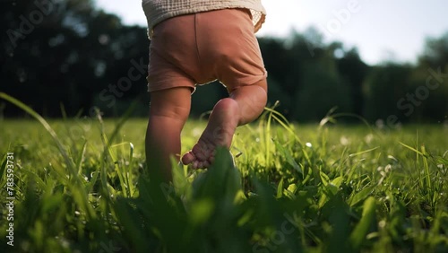First steps. Father's Day.father helps his baby son take his first steps on grass in tpark at sunset. Happy family concept.Dad and son outdoors in summer.Father teaches his son to take his first steps photo