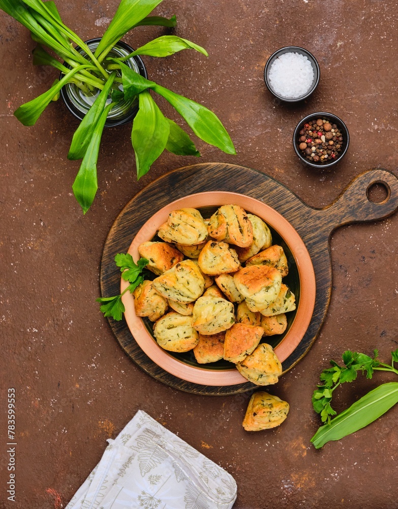 Unsweetened curd cookies with parsley and wild garlic in a ceramic plate on a brown concrete background. Baking with herbs, wild garlic recipes. Unsweetened curd cookies with parsley and wild garlic in a ceramic plate on a brown concrete background. Baking with herbs, wild garlic recipes.