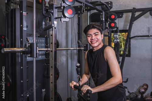 A young asian man does a set of straight bar tricep pushdowns. A first time beginner tries to building muscle mass on his arms and upper torso. Modern gym setting.