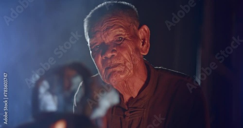  Asian rural life at dawn which is a poor elderly farmer man and worker in the rural farm, boiling water with an old kettle using a stove with firewood, boiling steam and smoke from firewood.