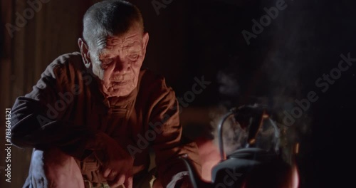  Asian rural life at dawn which is a poor elderly farmer man and worker in the rural farm, boiling water with an old kettle using a stove with firewood, boiling steam and smoke from firewood. photo