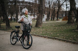 Mature woman stands with her bike in a park, showcasing an active lifestyle and leisure time outdoors.