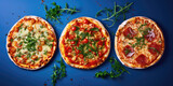 Three different pizzas with assorted toppings and melted cheese, garnished with fresh herbs, displayed on a blue background.