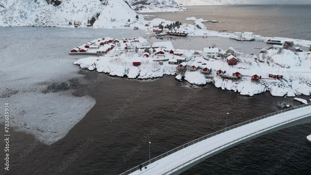 Drohnenaufnahme von Hamnoy, Schwenk nach oben, rote Häuser mit schneebedeckten Dächern, gefrorenes Meer, Blick auf gesamte Küste 